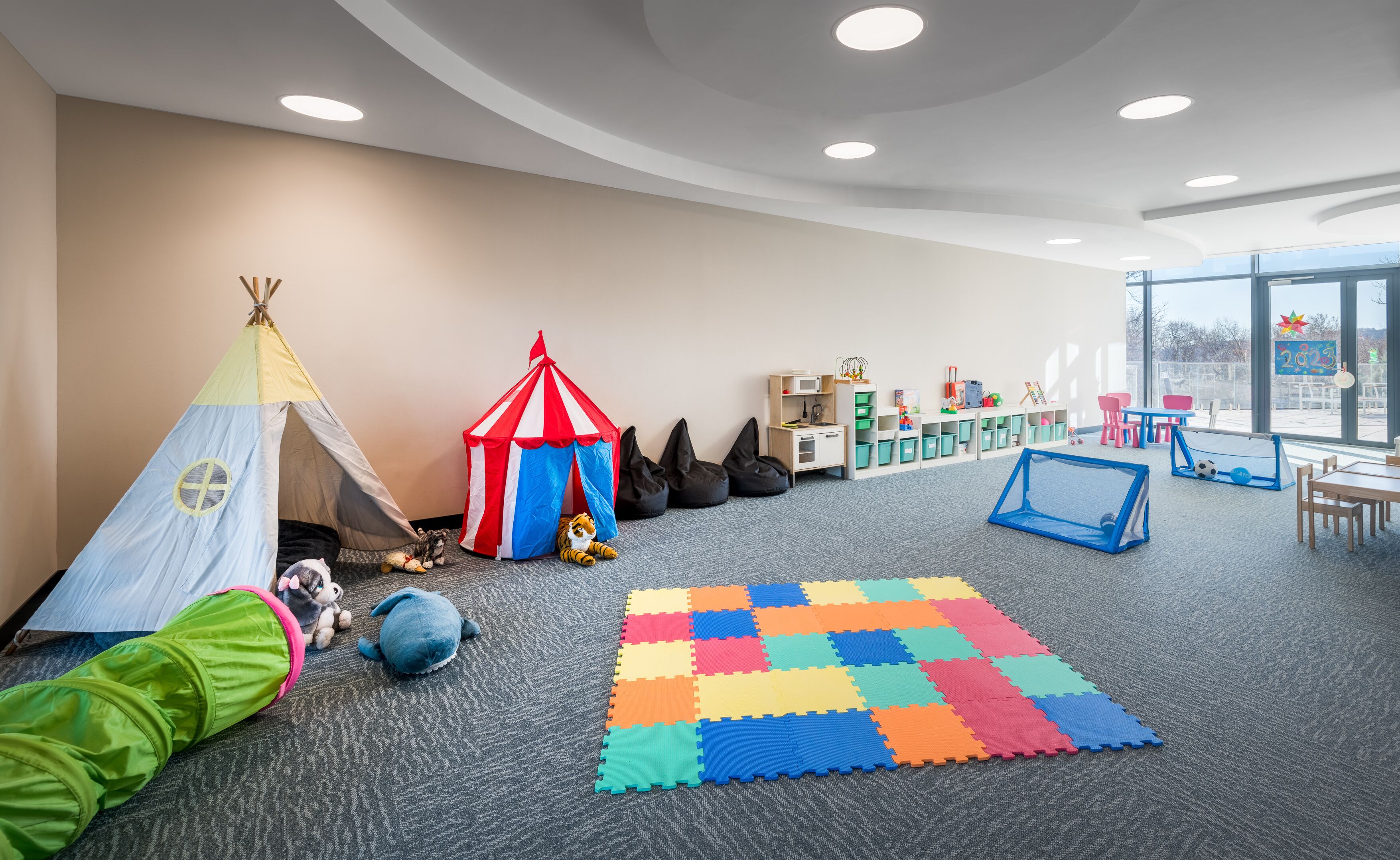 A children's play area with a tent, playhouse, bean bags, and a colorful play mat.