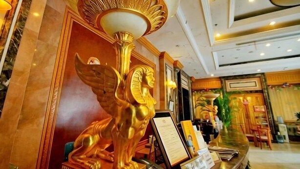 Een lobby met een gouden standbeeld, een receptiebalie en een kroonluchter.