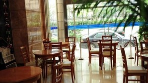 Een café met houten tafels en stoelen, een betegelde vloer en uitzicht op een straat met auto's en groen.