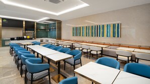 A modern dining area with multiple tables and chairs, a kitchen in the background, and a colorful abstract painting on the wall. - Yizhi Hotel (Dongshankou Subway Station Store, First Affiliated Hospital of Sun Yat sen University) (Guangzhou)
