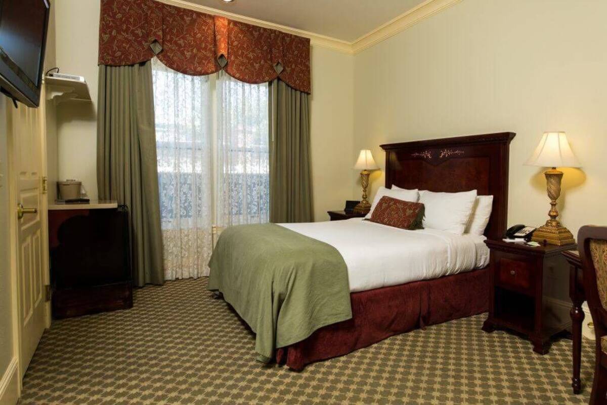 A hotel room with a large bed, two bedside lamps, a nightstand, a dresser, and a window with curtains.