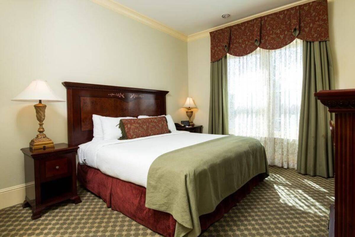 A neatly made bed with a wooden headboard, two bedside tables with lamps, and a window with curtains.