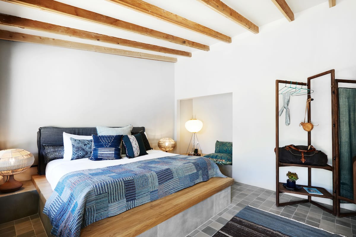 Une chambre à coucher avec un lit, une table de chevet, une lampe et un banc en bois.