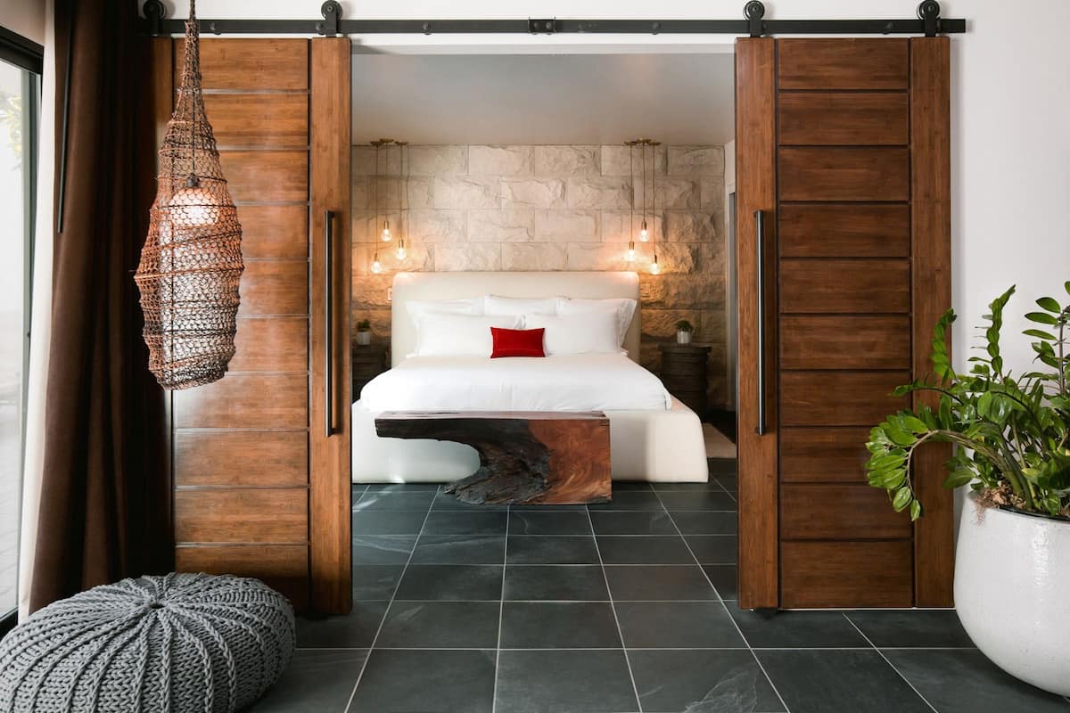Une chambre à coucher avec un lit, une tête de lit en bois, un luminaire suspendu et une plante en pot.