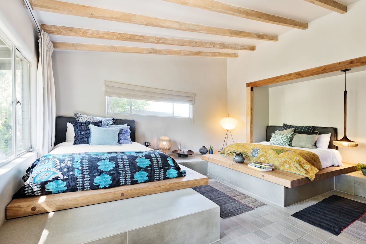 Une chambre avec un grand lit, un plus petit lit, une fenêtre et une table de chevet avec une lampe.