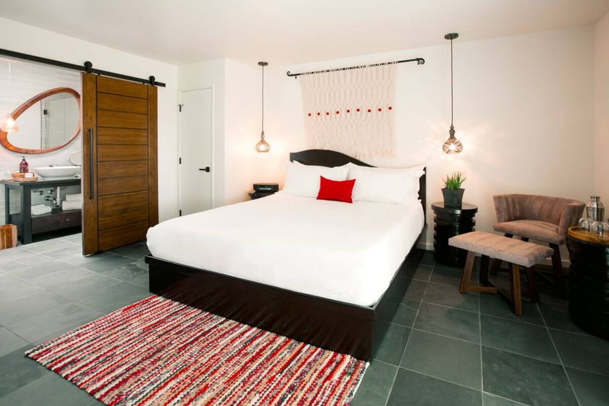 Une chambre moderne avec un grand lit, une porte coulissante en bois, une table de chevet avec une lampe, une chaise et une petite table avec une plante.