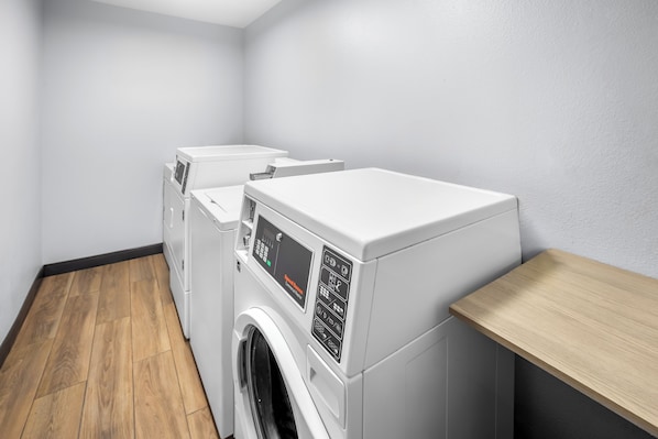 A laundry room with two washing machines and a wooden shelf.