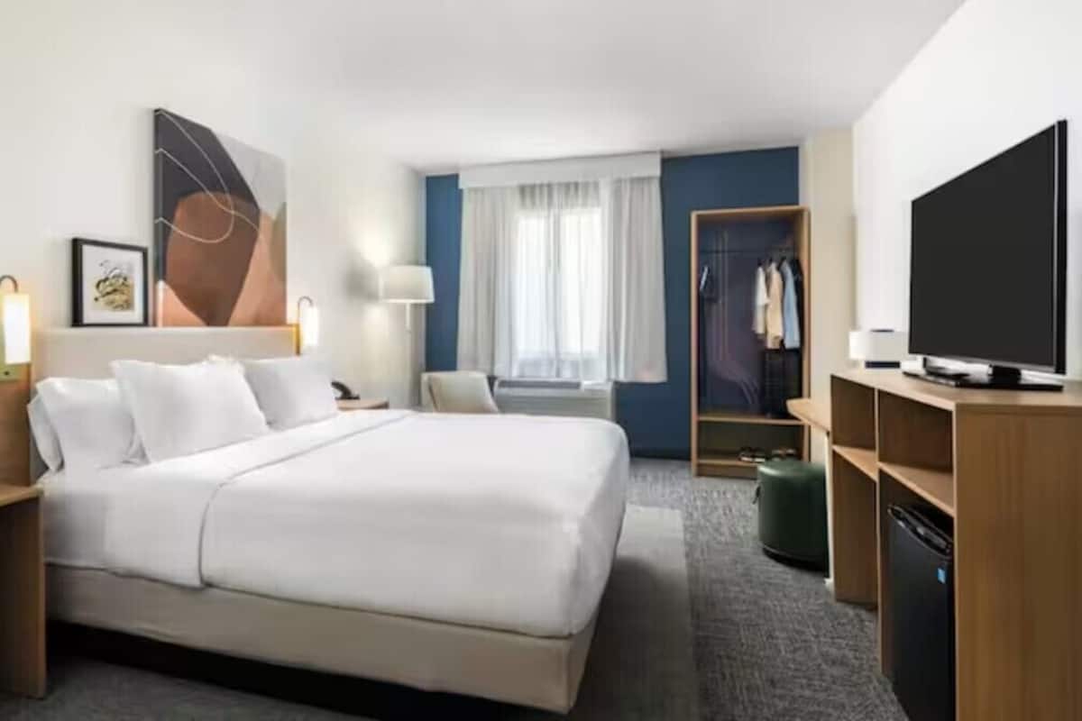 Hotelkamer met een groot bed, nachtkastjes, een televisie, een kledingkast en een raam met gordijnen.