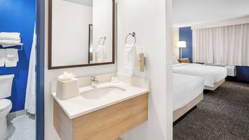 Una habitación de hotel con baño, una cama, una mesita de noche y un velador.