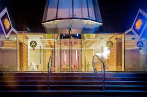 A hotel entrance with a glass facade, a central atrium, and a staircase leading up. - Avenue Hotel (Dubai)