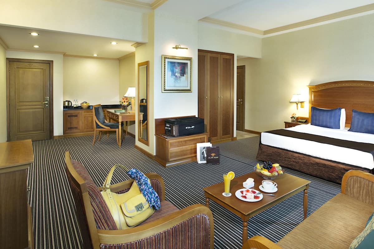 A hotel room with a large bed, a desk with a chair, a sofa, and a small table with breakfast items.