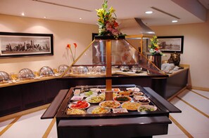 A buffet setup with various dishes and a central floral arrangement. - Avenue Hotel (Dubai)