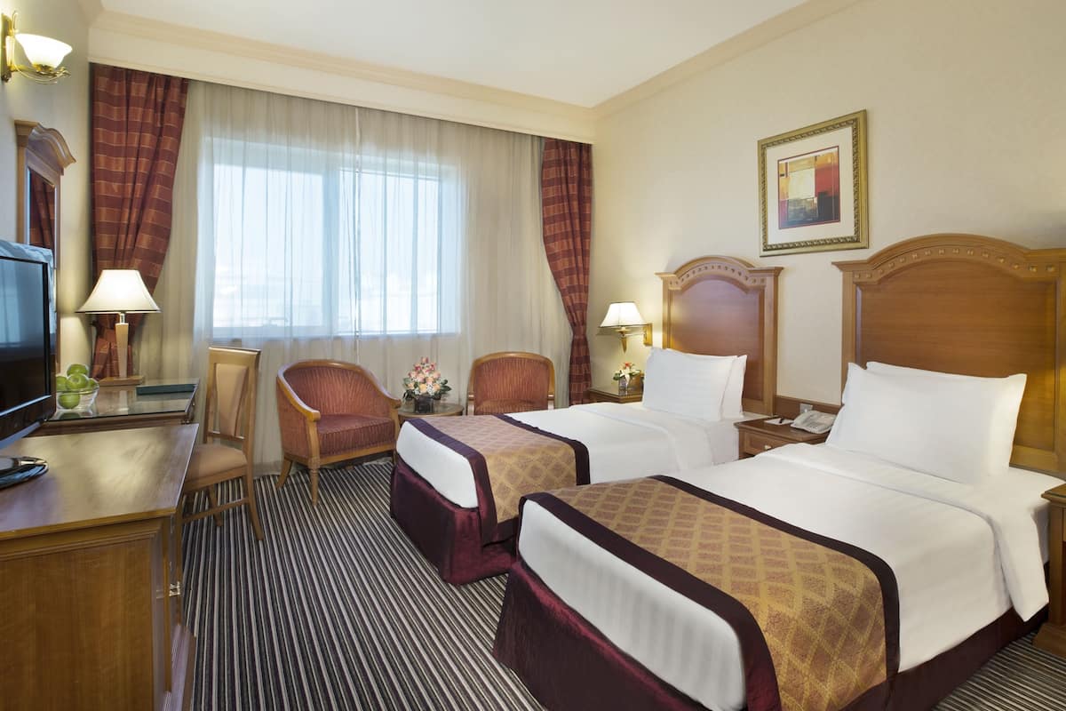 A hotel room with two beds, a desk with a television, and a window with curtains.