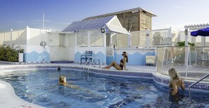 A swimming pool with tiled edges, a covered seating area, and a building with solar panels. - Avenue Hotel (Dubai)