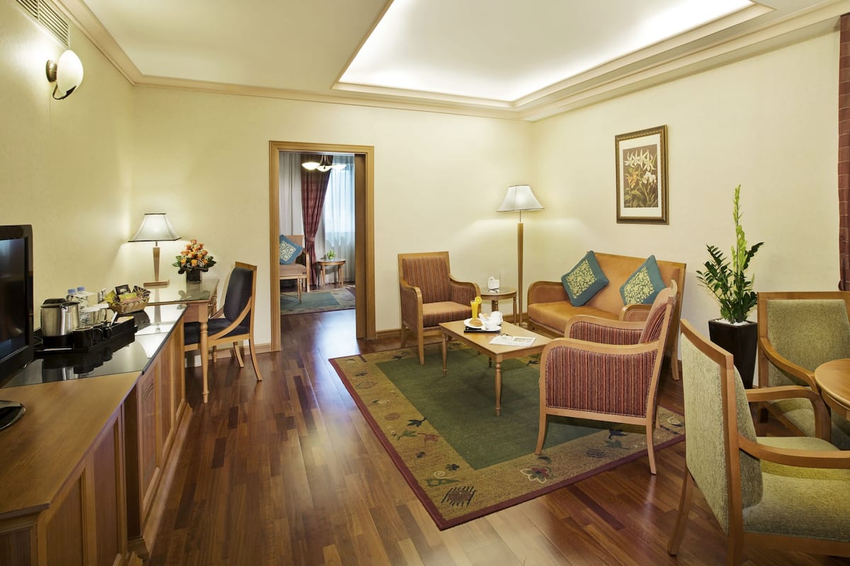 A hotel room with a dining area, a sofa set, a coffee table, a TV, and a plant.