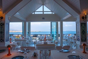 A restaurant with tables set for dining, large windows offering a view of the sea and cityscape. - Avicenna Hotel - Special Class (Istanbul)