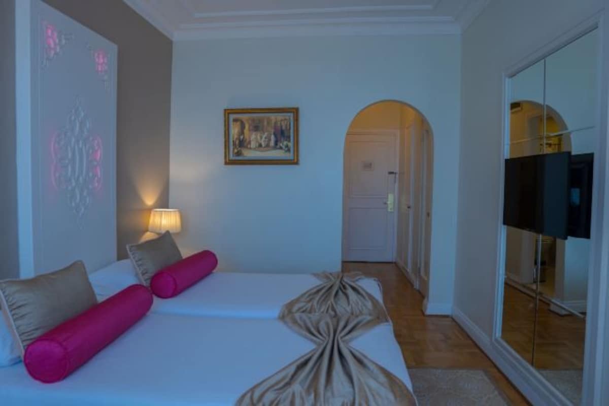 Habitació d'hotel amb un llit, una televisió, un quadre i una porta que dona a una altra habitació.
