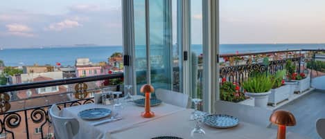 A dining area with a table set for two, overlooking a coastal cityscape.