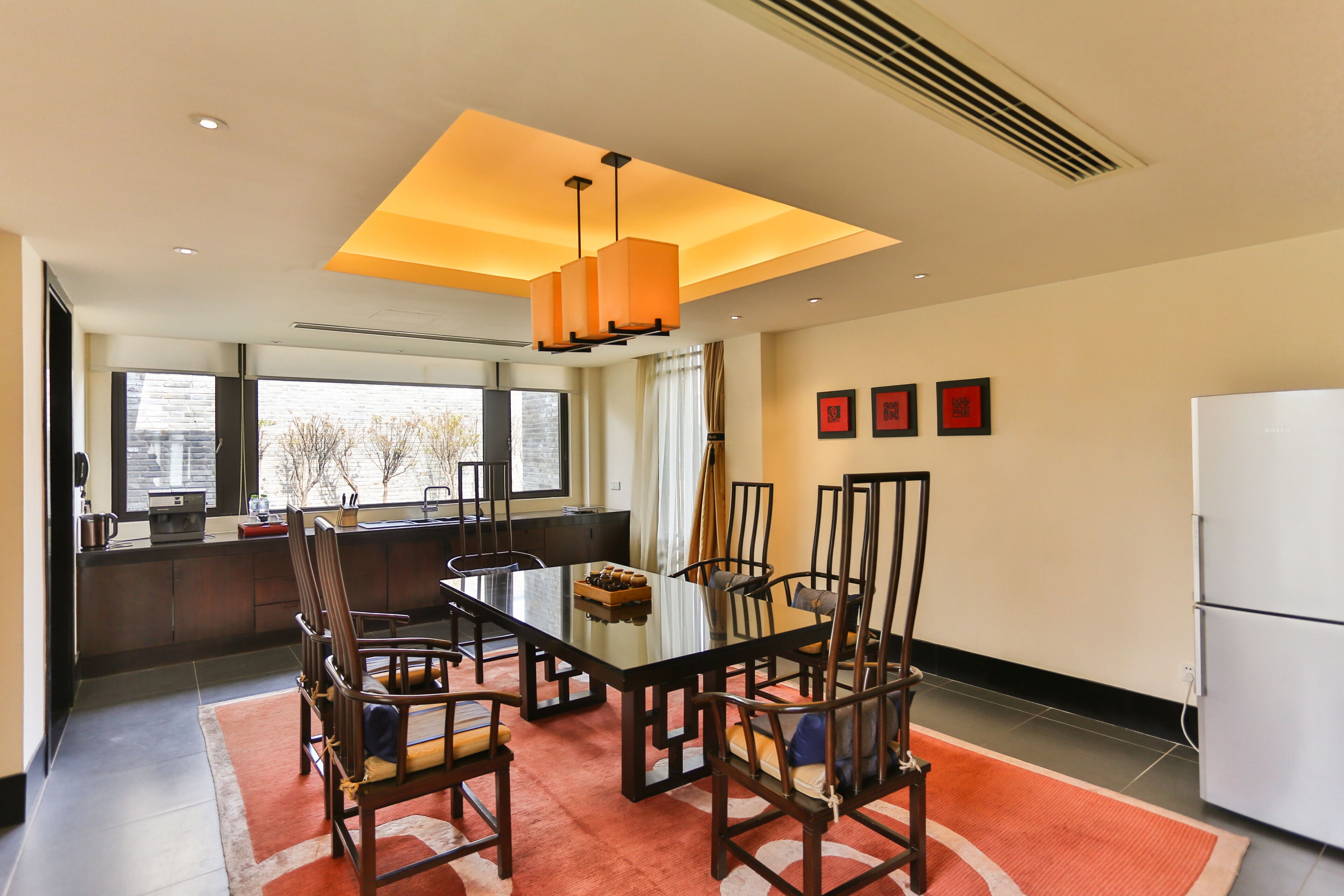 A modern dining area with a glass table, wooden chairs, and a central light fixture.