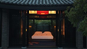 Una habitación de estilo tradicional con una cama centrada en un cabecero de madera, rodeada de paredes oscuras y un techo de tejas.