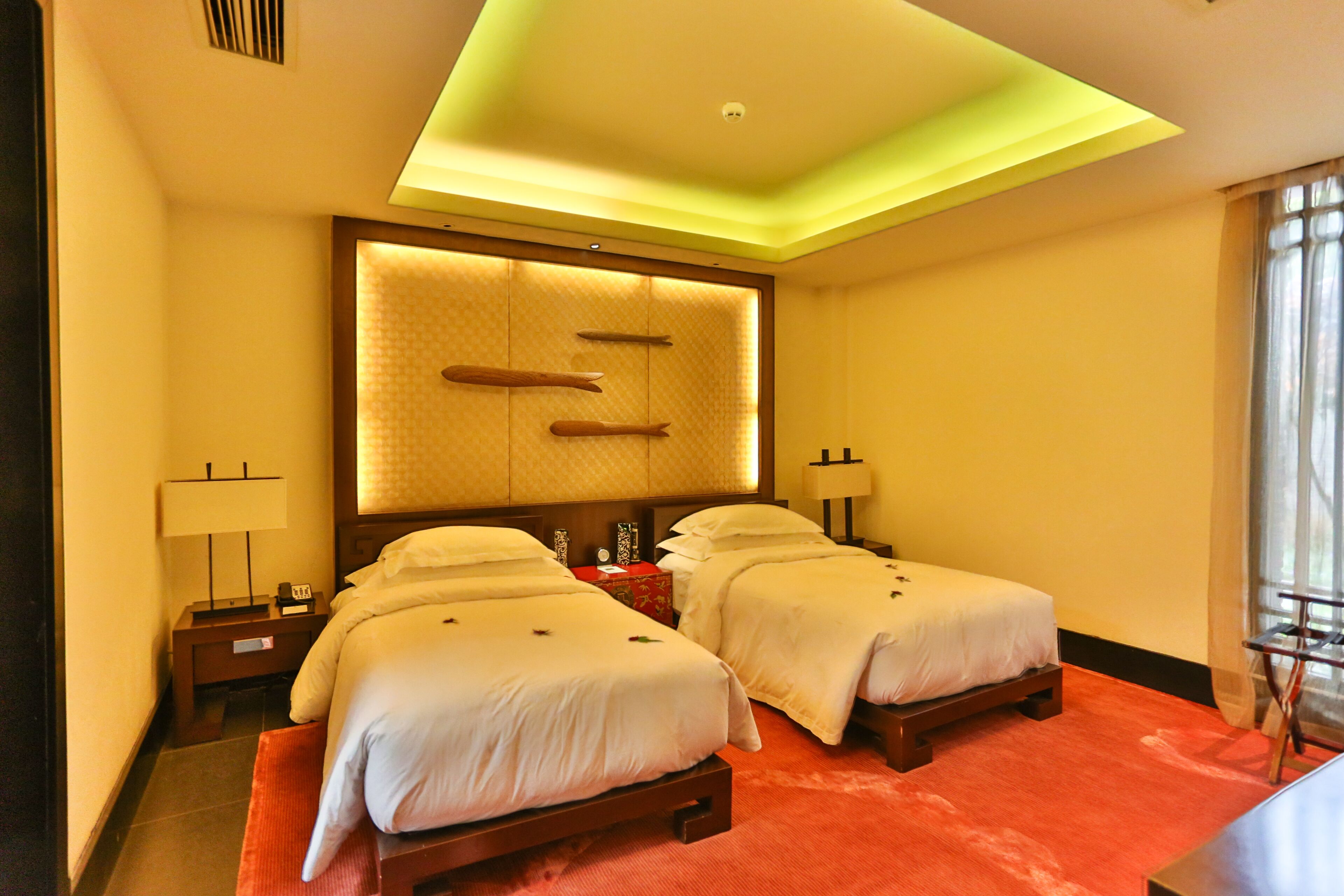 A hotel room with two beds, a large wall-mounted headboard, bedside lamps, and a red carpet.