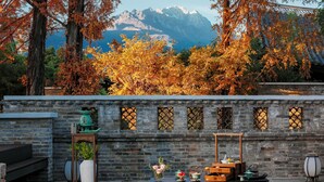 Un espacio de estar al aire libre de estilo tradicional, con un muro de piedra, una mesa con un jarrón de flores y vistas al follaje otoñal y montañas.