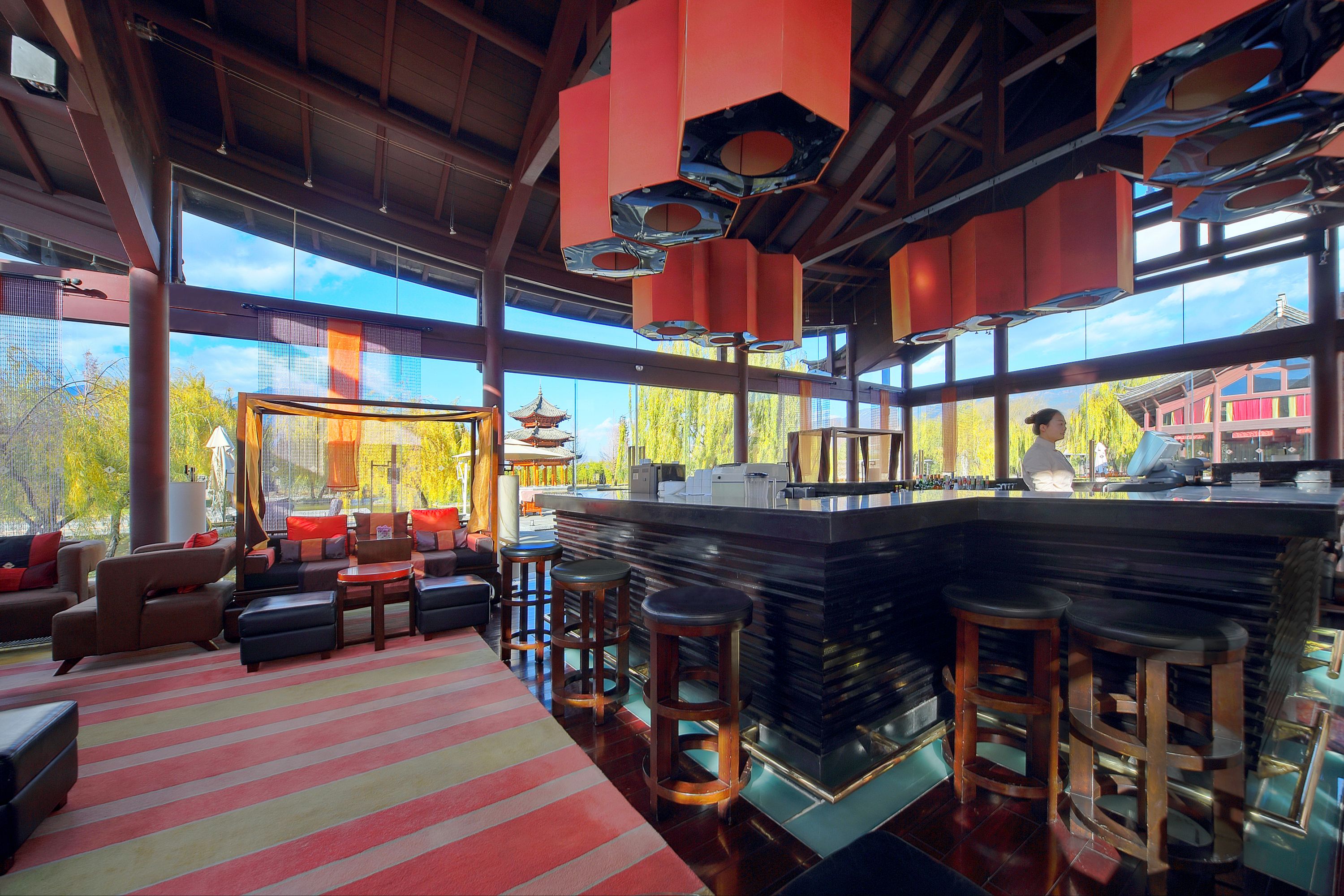 Een moderne bar met een hoge toog, meerdere krukken, en een zithoek met banken en een getextureerd vloerkleed.