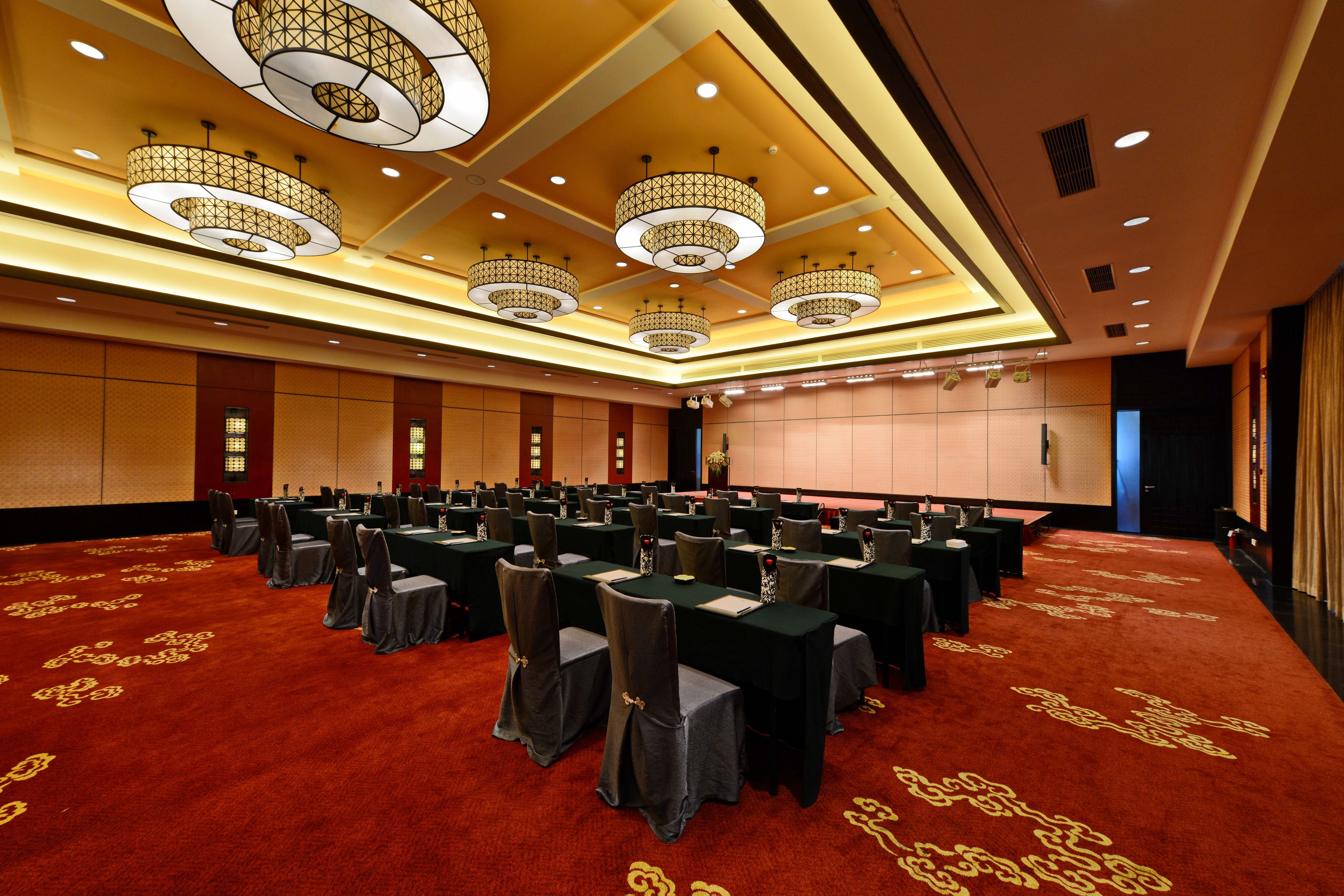 A conference room with multiple tables and chairs, large chandeliers, and a red carpeted floor.