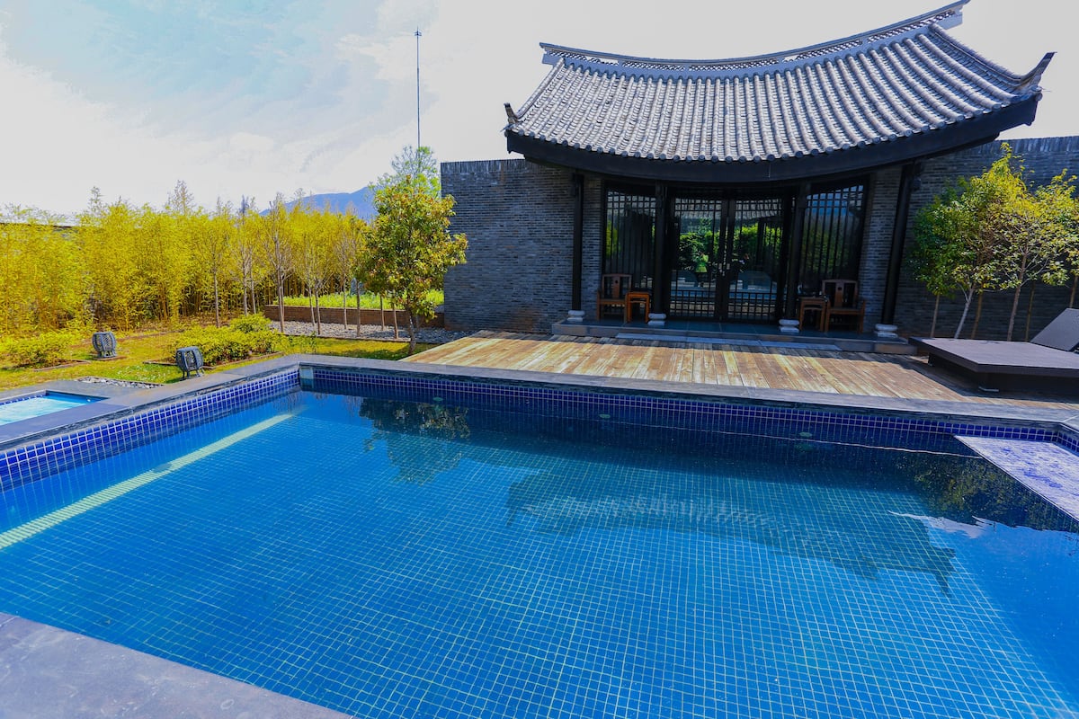 Una piscina con bordes de azulejos, una cubierta de madera y un edificio tradicional con techo curvo.