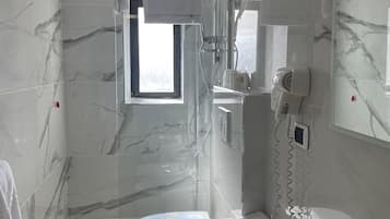 Un bagno moderno con rivestimento in marmo, doccia con porta in vetro, WC, lavandino e asciugacapelli.