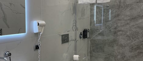 Une salle de bain moderne avec un pare-baignoire en marbre, un lavabo blanc, un bidet et une douche à l’italienne.
