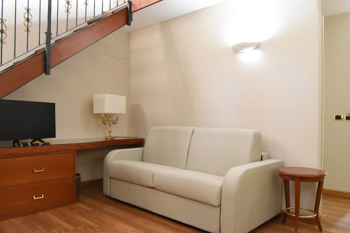 Una habitación con una escalera de madera, un sofá blanco, una pequeña mesa de madera y un televisor sobre un mueble de madera.