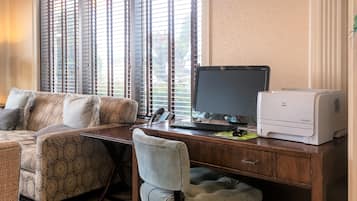 A home office with a desk, computer, printer, and a sofa with patterned cushions.