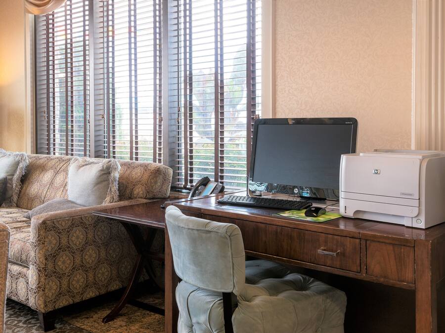 A home office with a desk, computer, printer, and a sofa with patterned cushions.