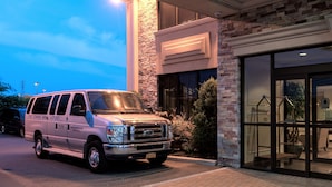 A light-colored SUV parked in front of a building with a stone facade and large windows. - Five Towns Inn - JFK Airport (Lawrence)