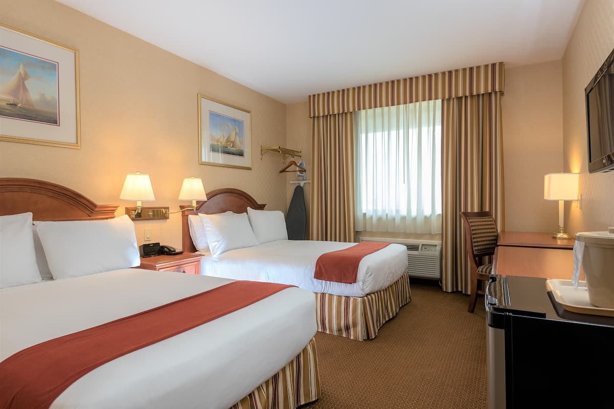 A hotel room with two beds, a desk, a chair, a lamp, and a window with curtains.