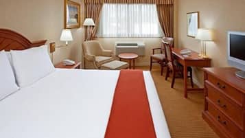 A hotel room with a large bed, a desk with a chair, a television, and a small table.
