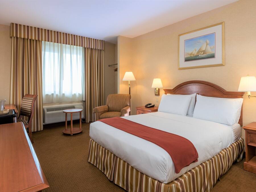 Een hotelkamer met een groot bed, twee bedlampen, een stoel, een bureau en een schilderij aan de muur.