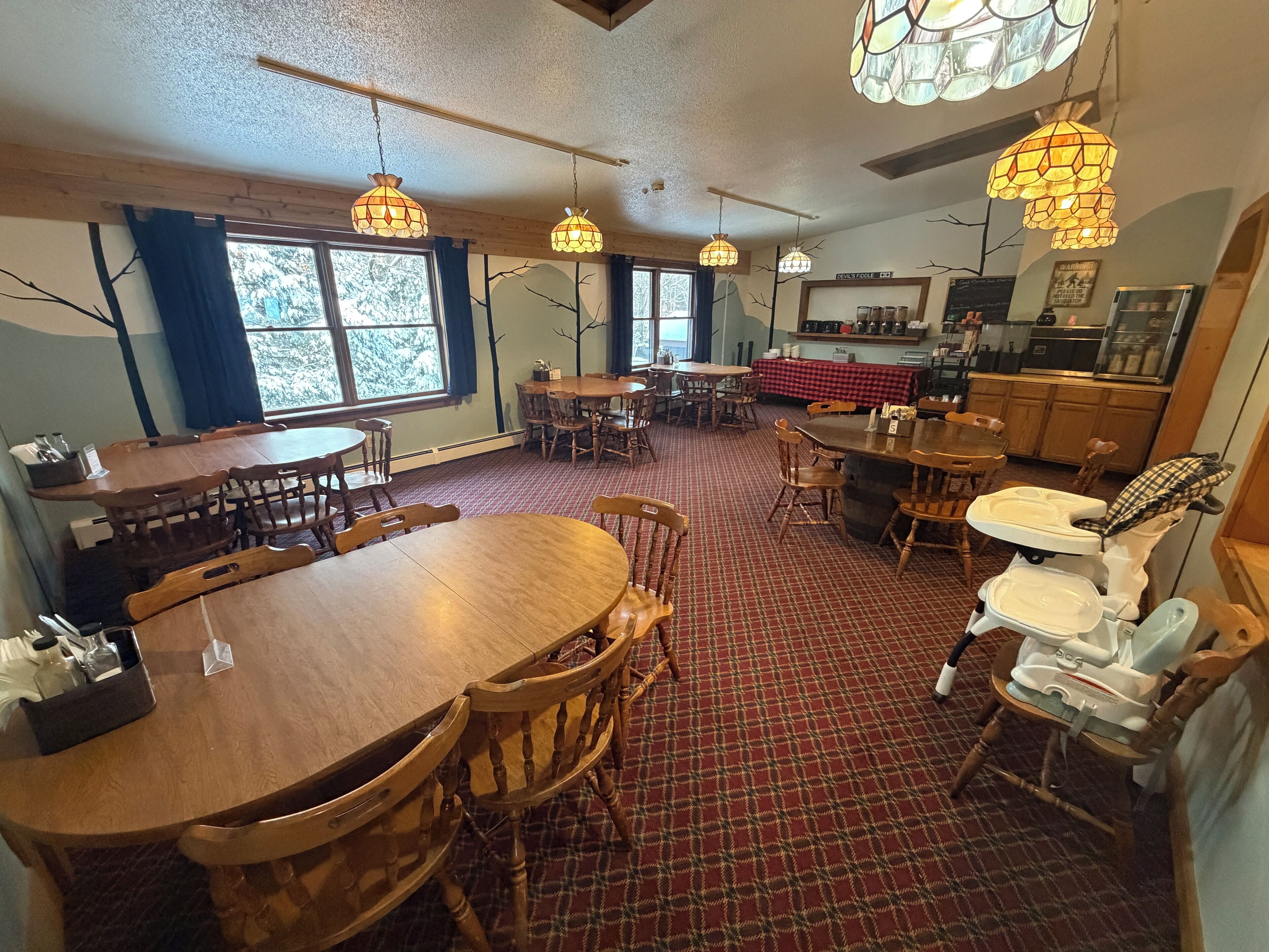 A dining area with wooden tables and chairs, a red checkered floor, and hanging pendant lights.