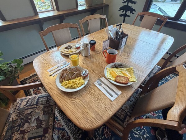 A wooden dining table with breakfast plates, utensils, and a coffee cup.