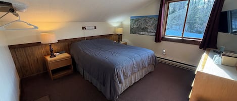 Une chambre d’hôtel avec un lit, des tables de chevet, une lampe, une fenêtre donnant sur des arbres et un tableau au mur.