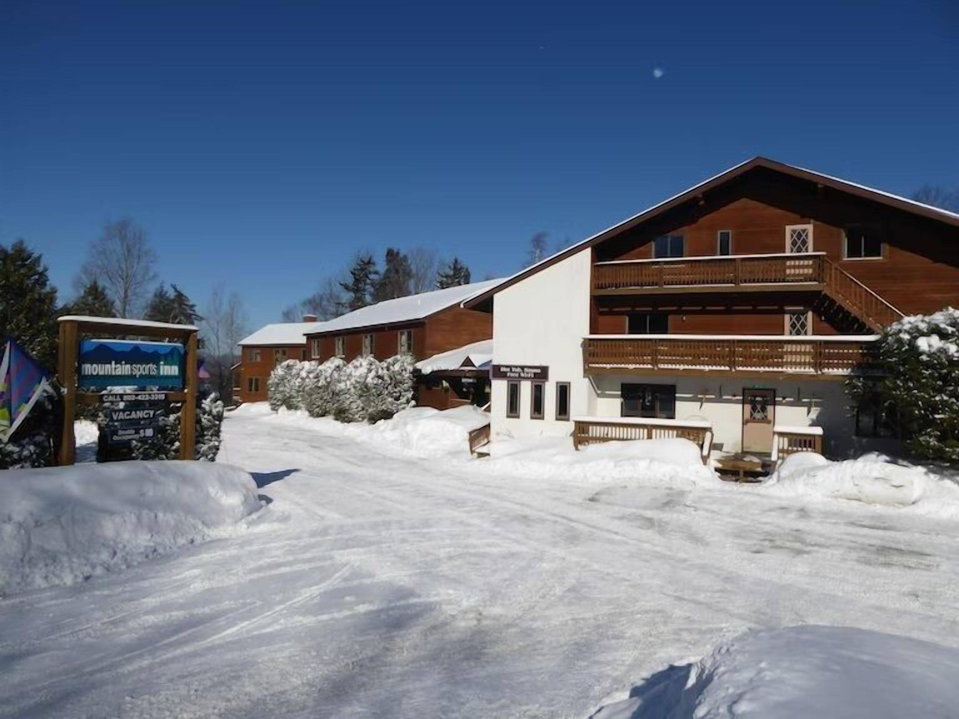 A large lodge with a wooden facade and a balcony, surrounded by snow.