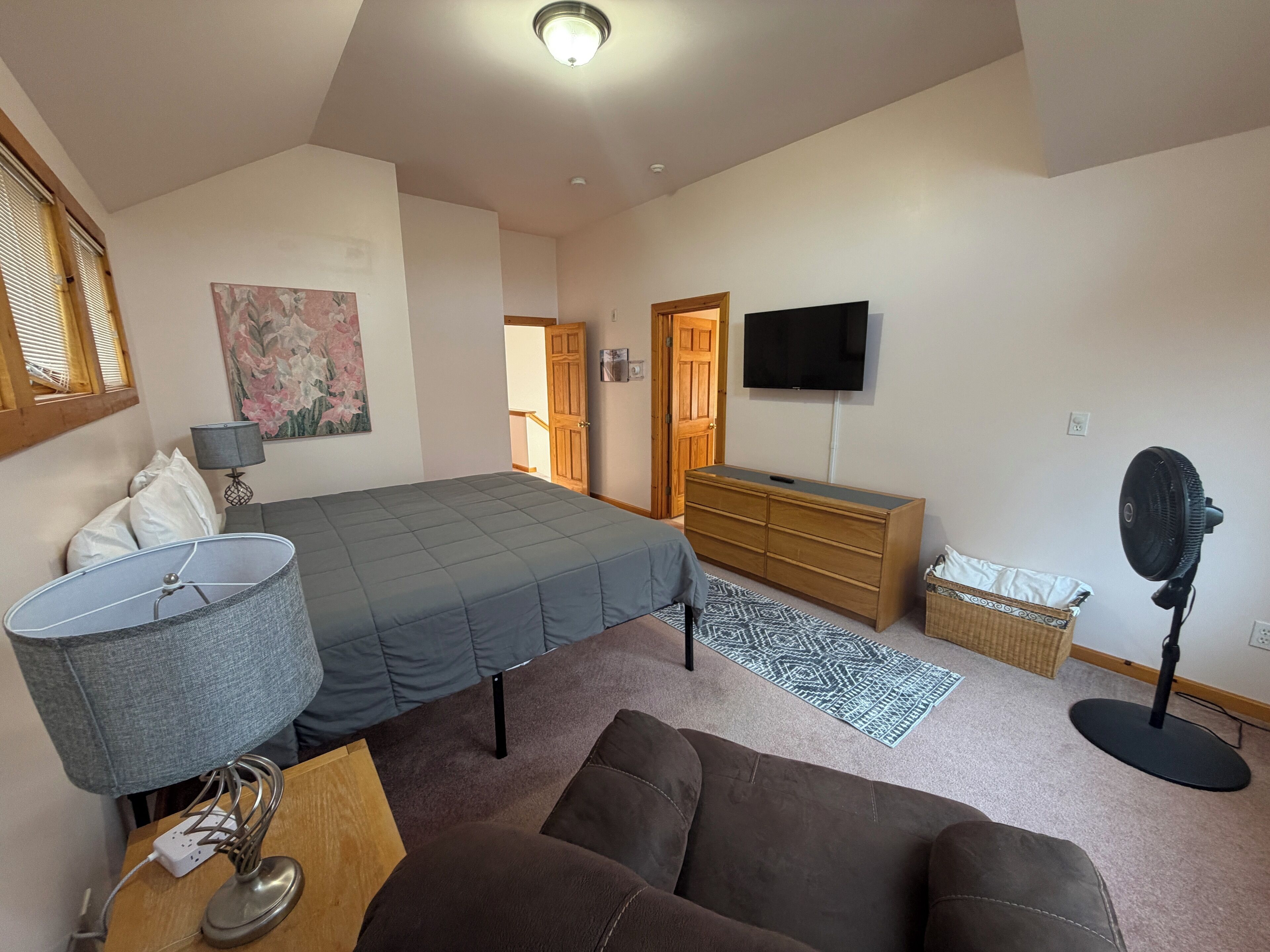 Une chambre à coucher avec un lit, une commode, une télévision, une lampe et un ventilateur.