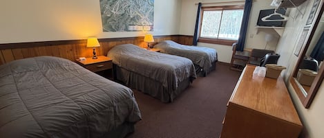 A hotel room with two beds, a wooden desk, a mirror, a window with curtains, and a map on the wall.