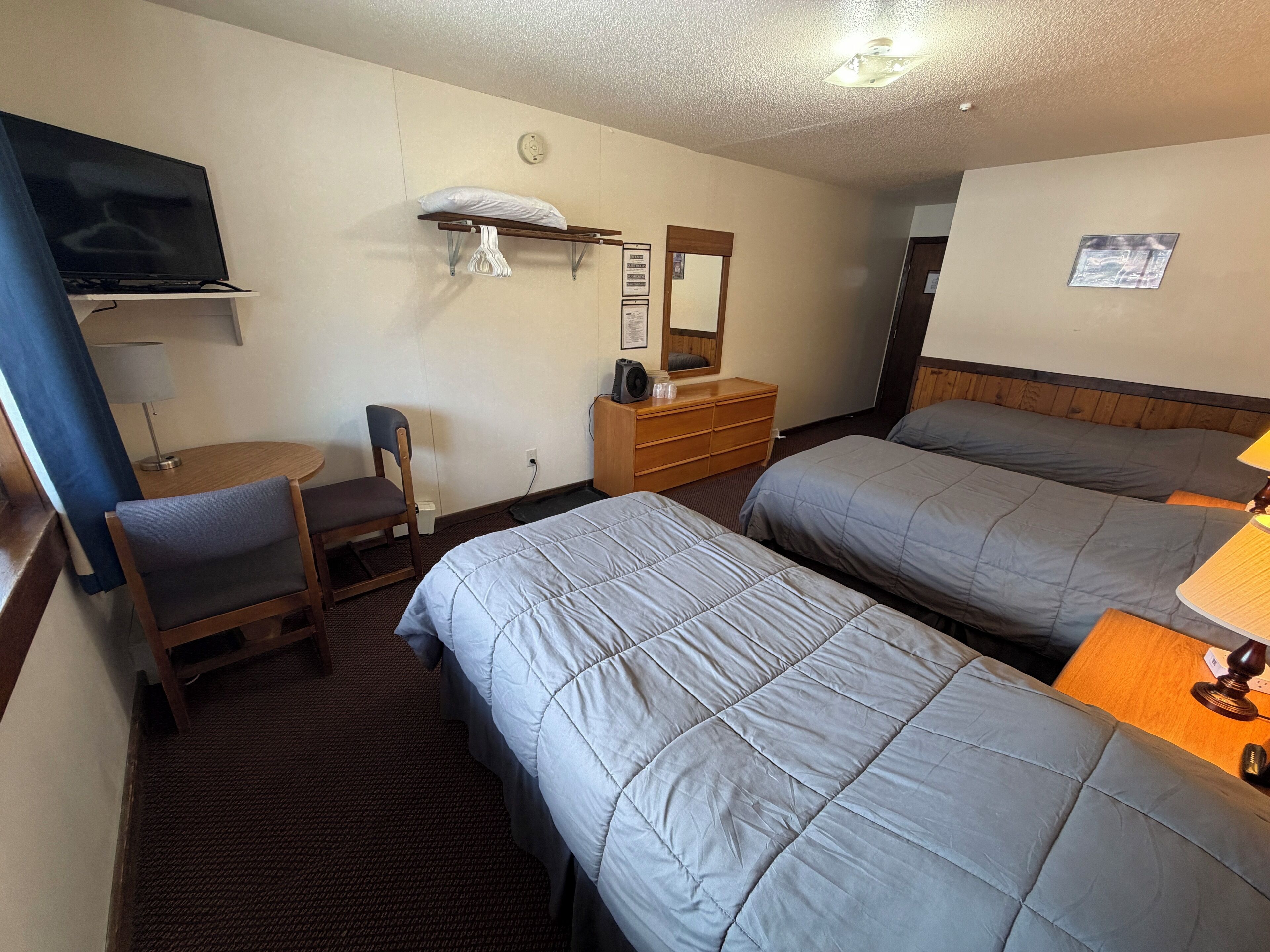 A hotel room with two beds, a desk with a chair, a TV, a dresser, and a mirror.