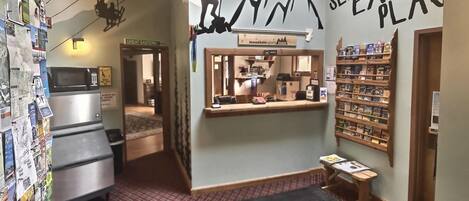 A hotel lobby with a ski-themed wall, a reception desk, a microwave, and a children's book shelf.