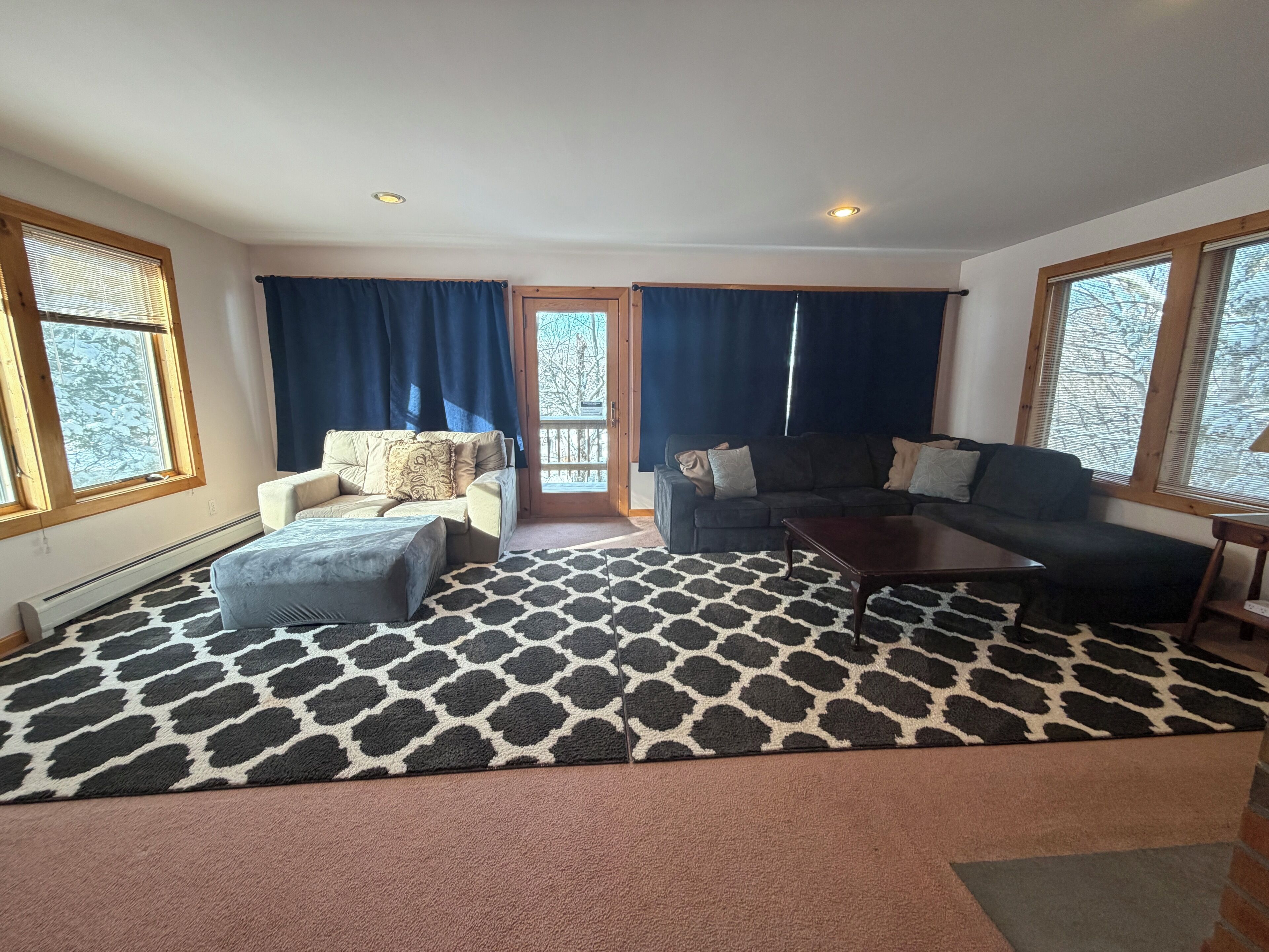 A living room with a patterned rug, two sofas, a coffee table, and large windows with curtains.