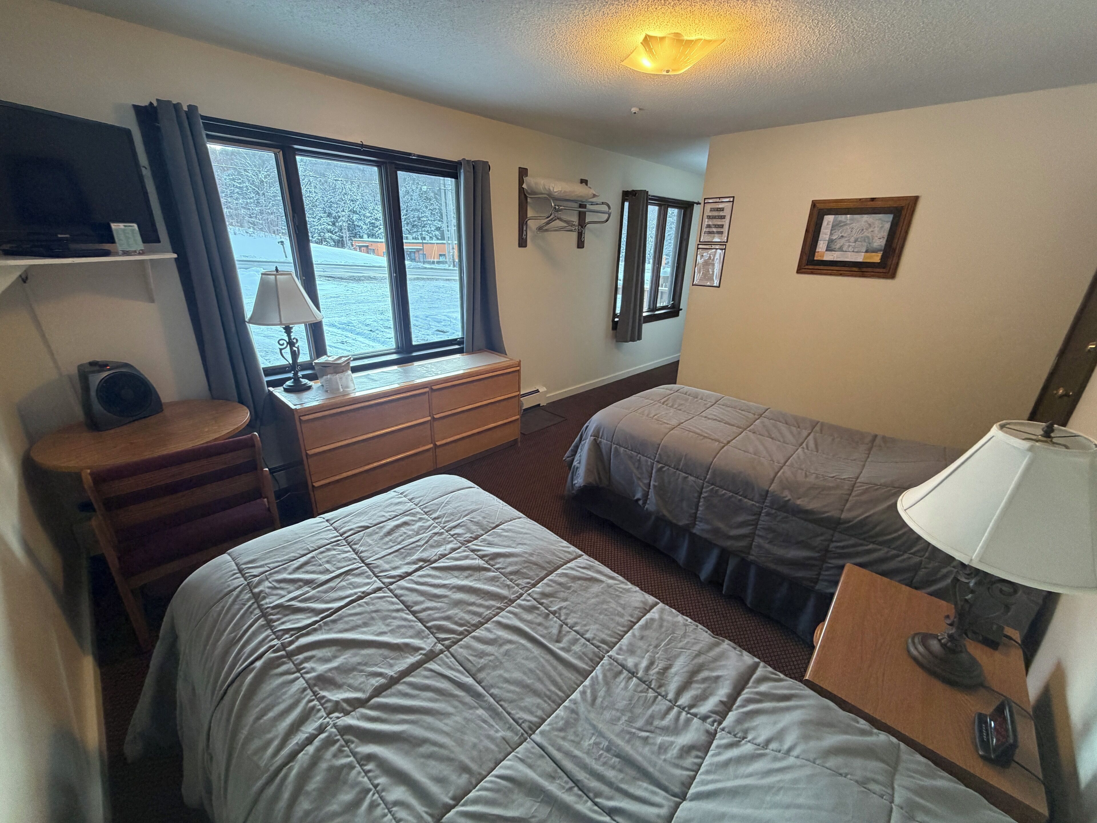 Habitación de hotel con dos camas, un escritorio, una silla, un televisor y una ventana con cortinas.
