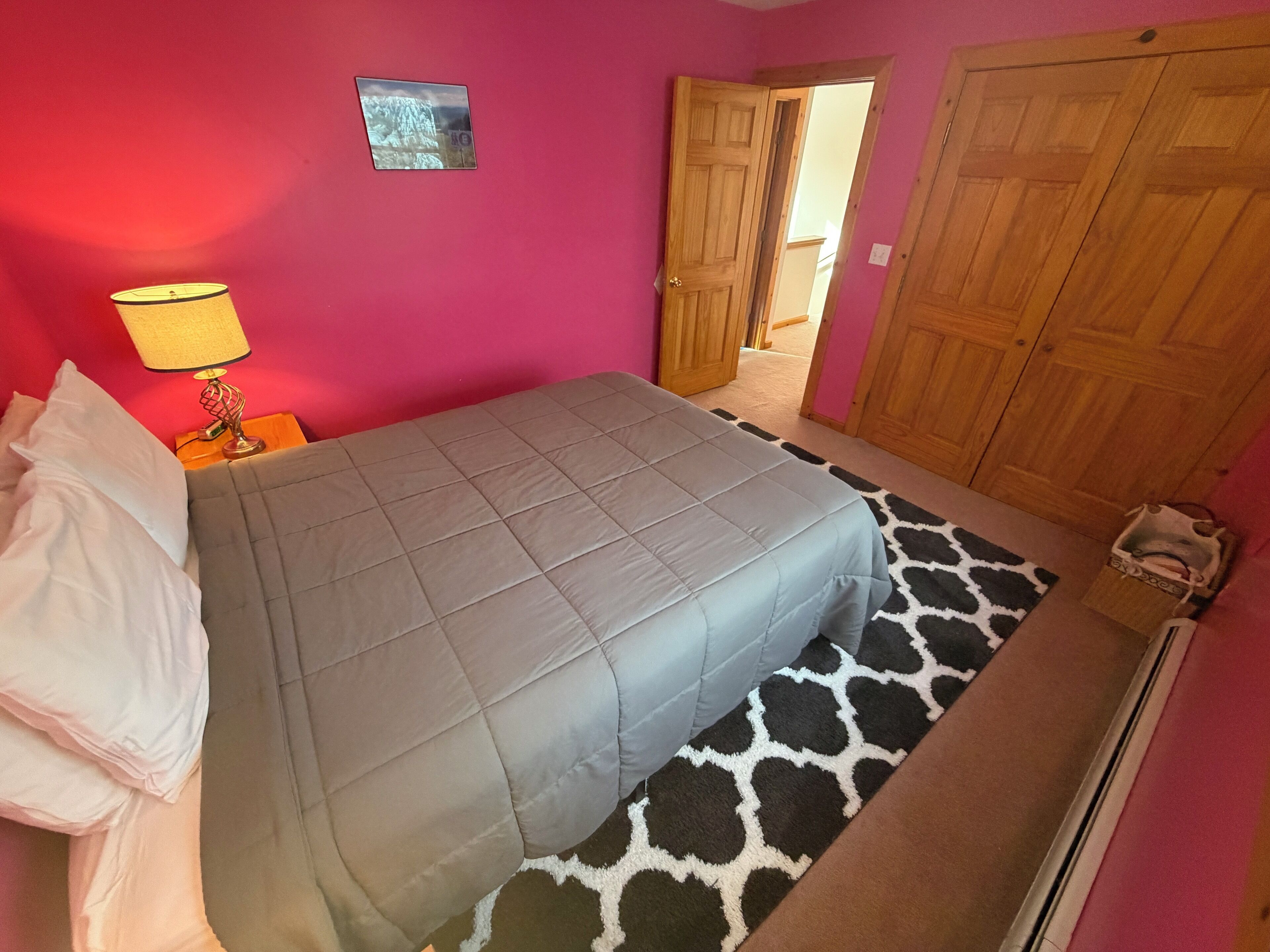 A bedroom with a bed, a nightstand, a lamp, a wardrobe, and a giraffe-patterned rug.