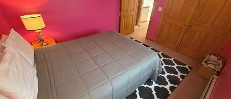 A bedroom with a bed, a nightstand, a lamp, a wardrobe, and a giraffe-patterned rug.